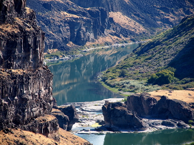 [The river curves into a wide area at the base of the canyon walls. There are many trees and grass in this area as well as several bridges across the water (but not across the canyon).]